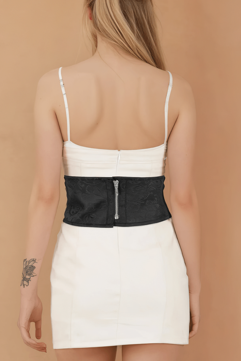 Back view of a model wearing a corset-inspired brocade belt with zip closure, styled with a white mini dress.