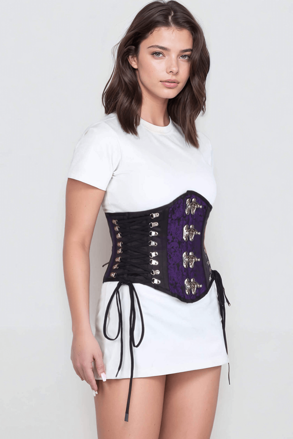 Model wearing purple brocade underbust corset with satin accents and tight lacing, highlighting stylish waist cinching.