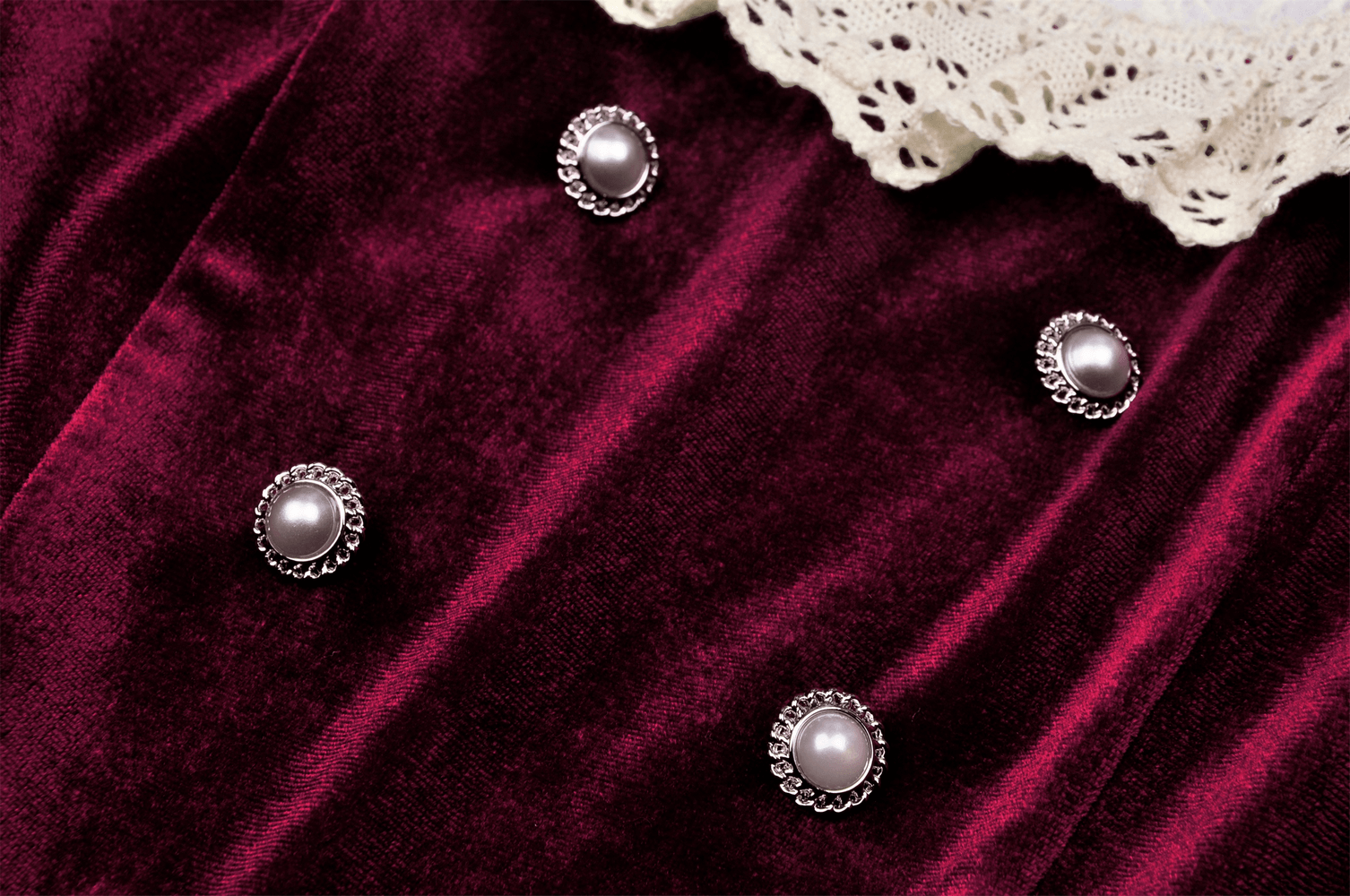 Close-up of burgundy velvet dress with pearl buttons and delicate lace collar accents, showcasing vintage elegance.