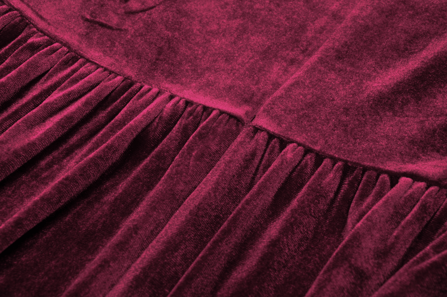 Close-up of burgundy velvet dress fabric with elegant pleats, highlighting luxurious texture and vintage charm.
