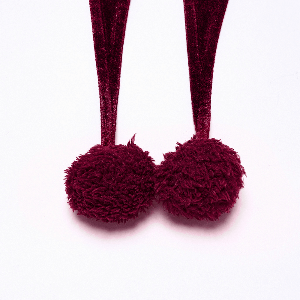 Burgundy velvet pom pom ties from a hooded cape, featuring fluffy texture and rich color.