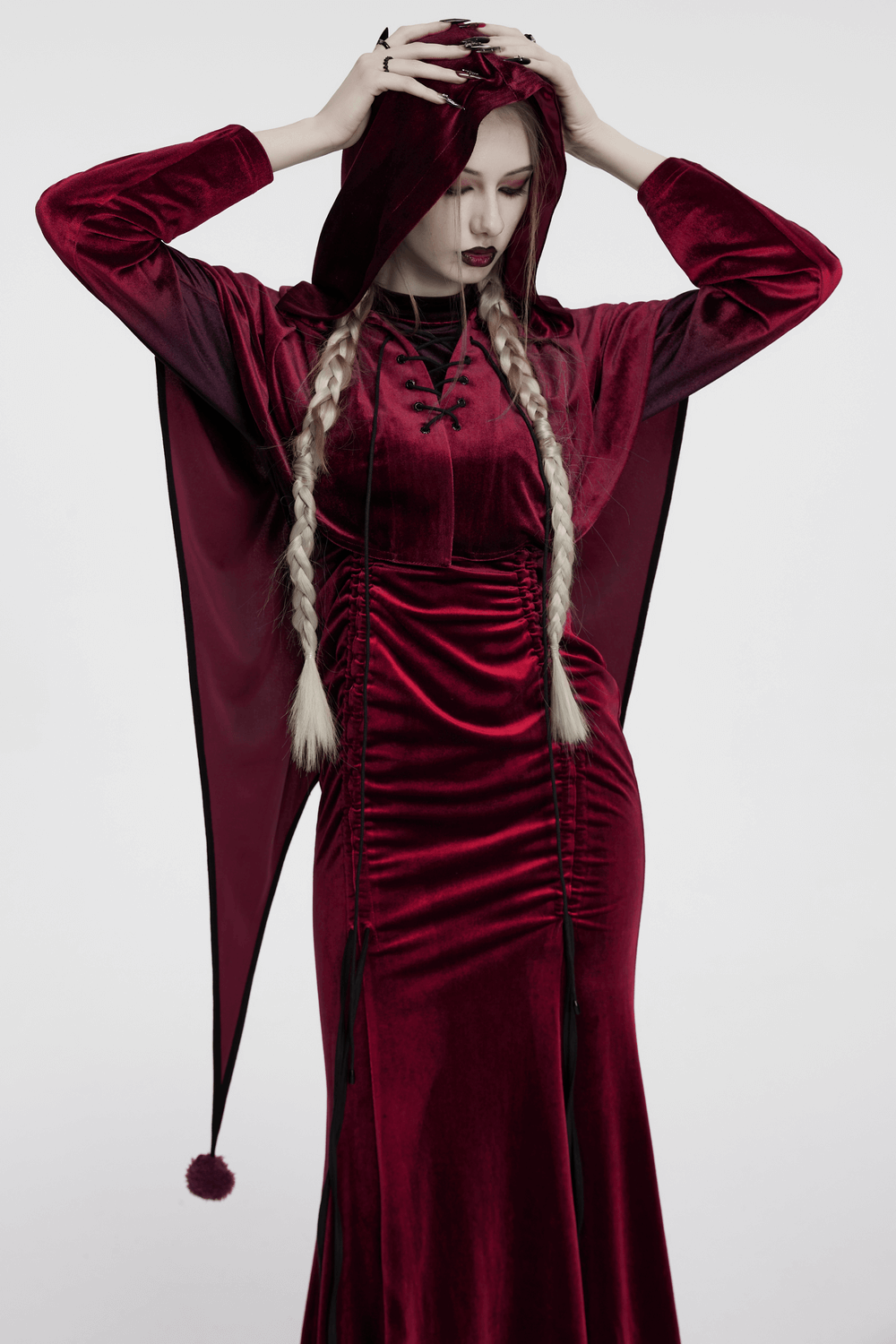 Burgundy velvet hooded cape with pom pom ties, featuring lace-up design and dramatic pointed hem.