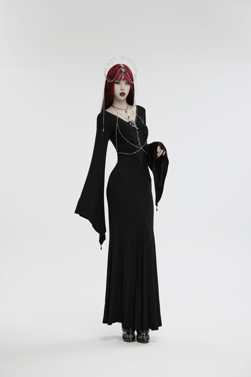 Model in black gothic dress wearing celestial headpiece with stars and moons, showcasing a mystical style.