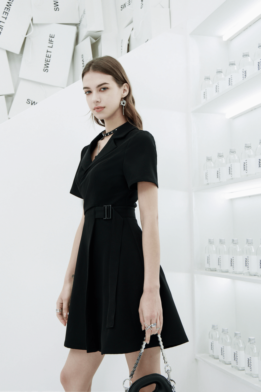 Chic A-Line dress with buckle detail and flared skirt, modeled in modern white setting with bottles.