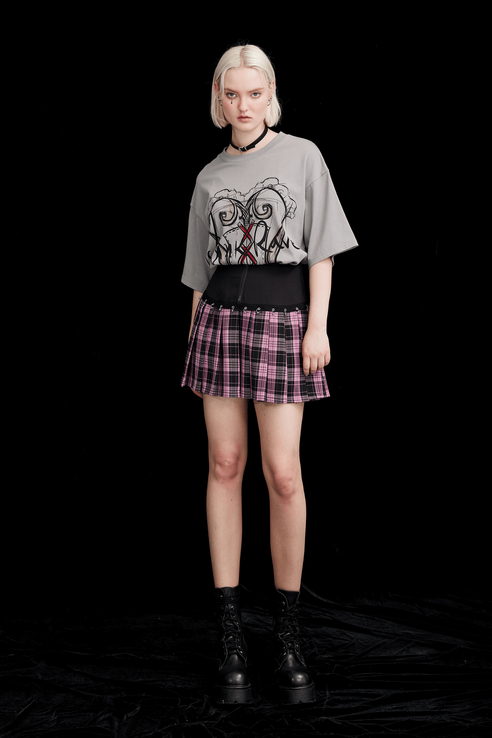Model wearing a chic A-line plaid skirt with metal ring accents and graphic tee, styled for trendy fashion lovers.