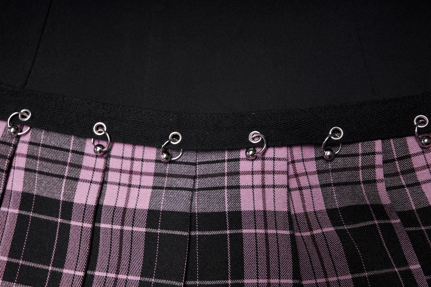 Close-up of a chic A-line plaid skirt showcasing metal ring accents and pleated design in pink and black.