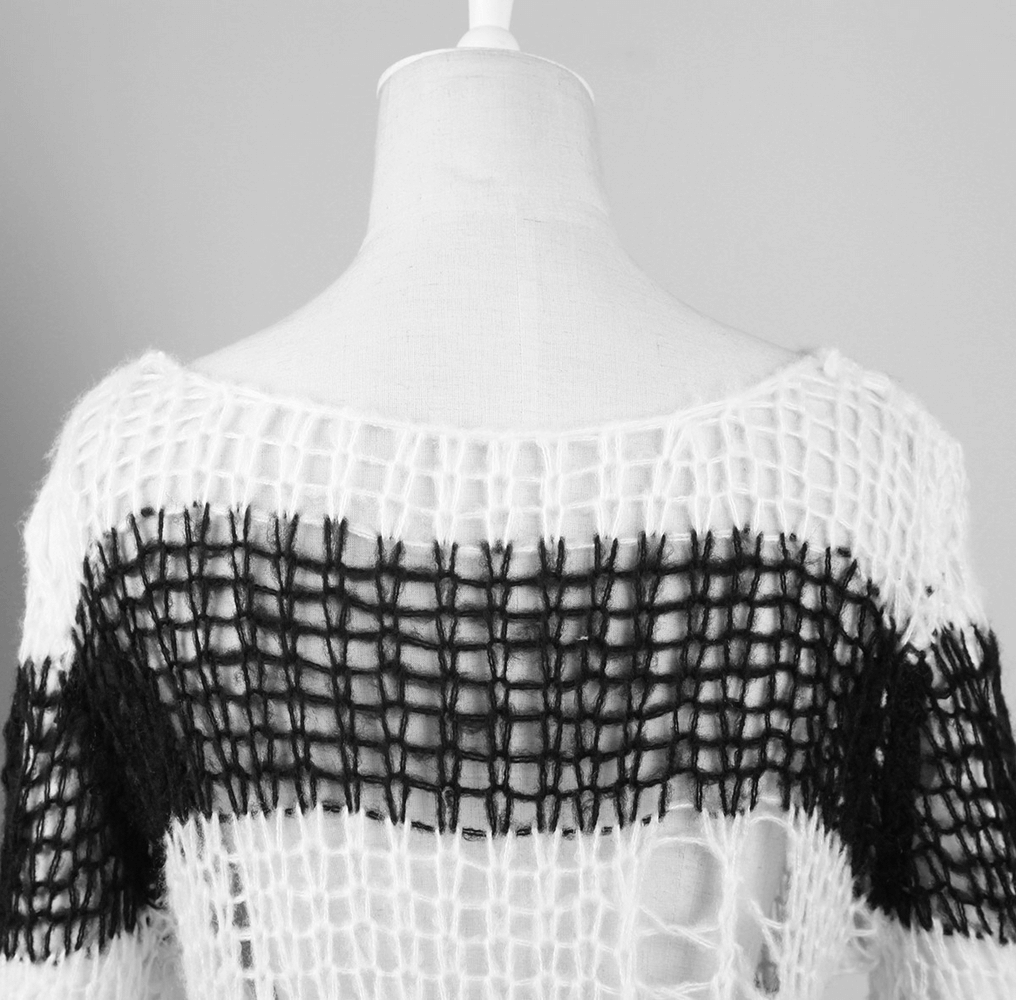 Back view of a chic black and white striped long sweater showcasing unique knit patterns and stylish holes.