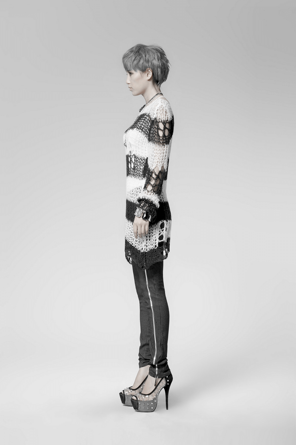 Chic black and white striped long sweater with holes, styled elegantly with high heels and skinny jeans.