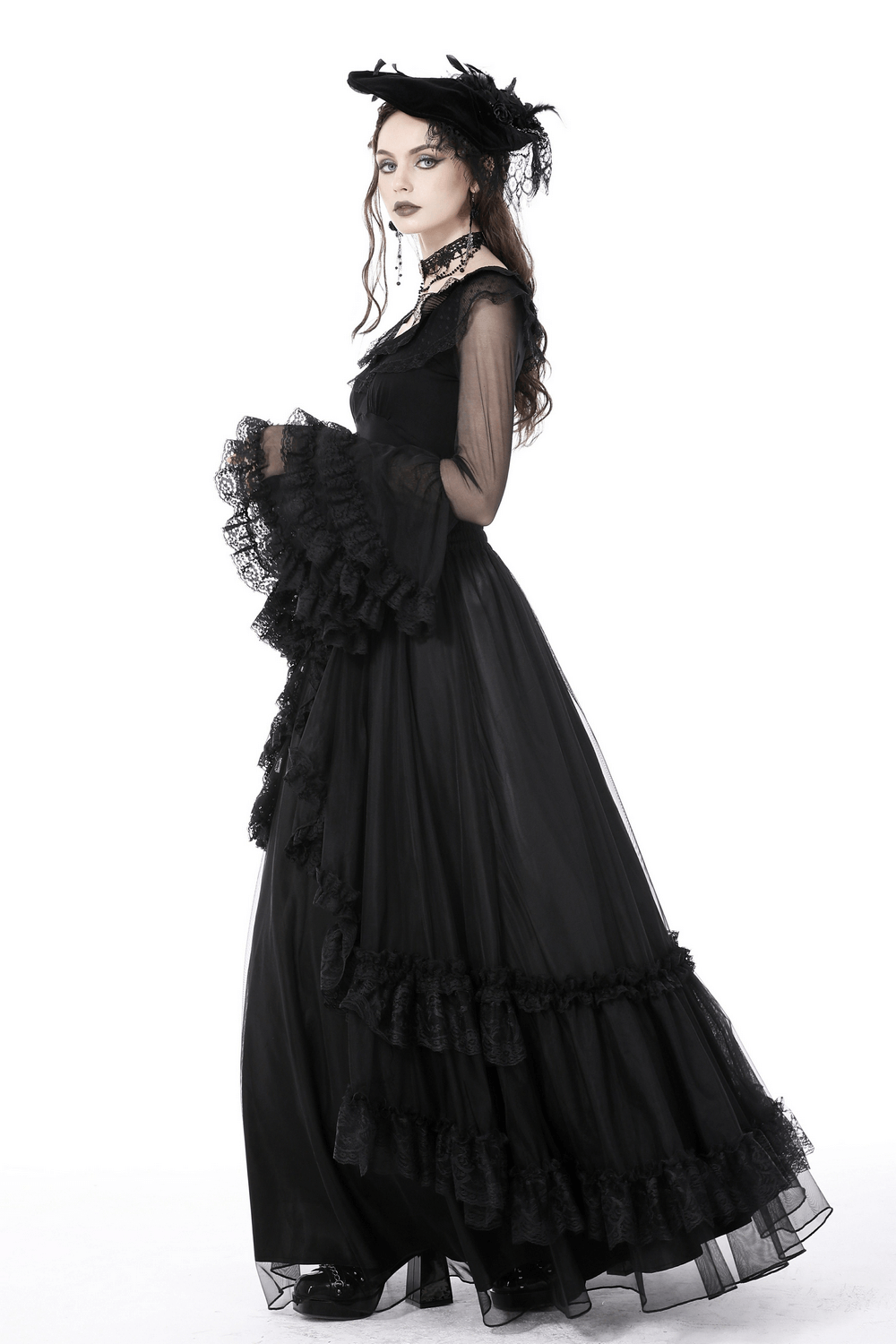 Gothic-inspired black lace gown with ruffled skirt and sheer bell sleeves, paired with a stylish hat.