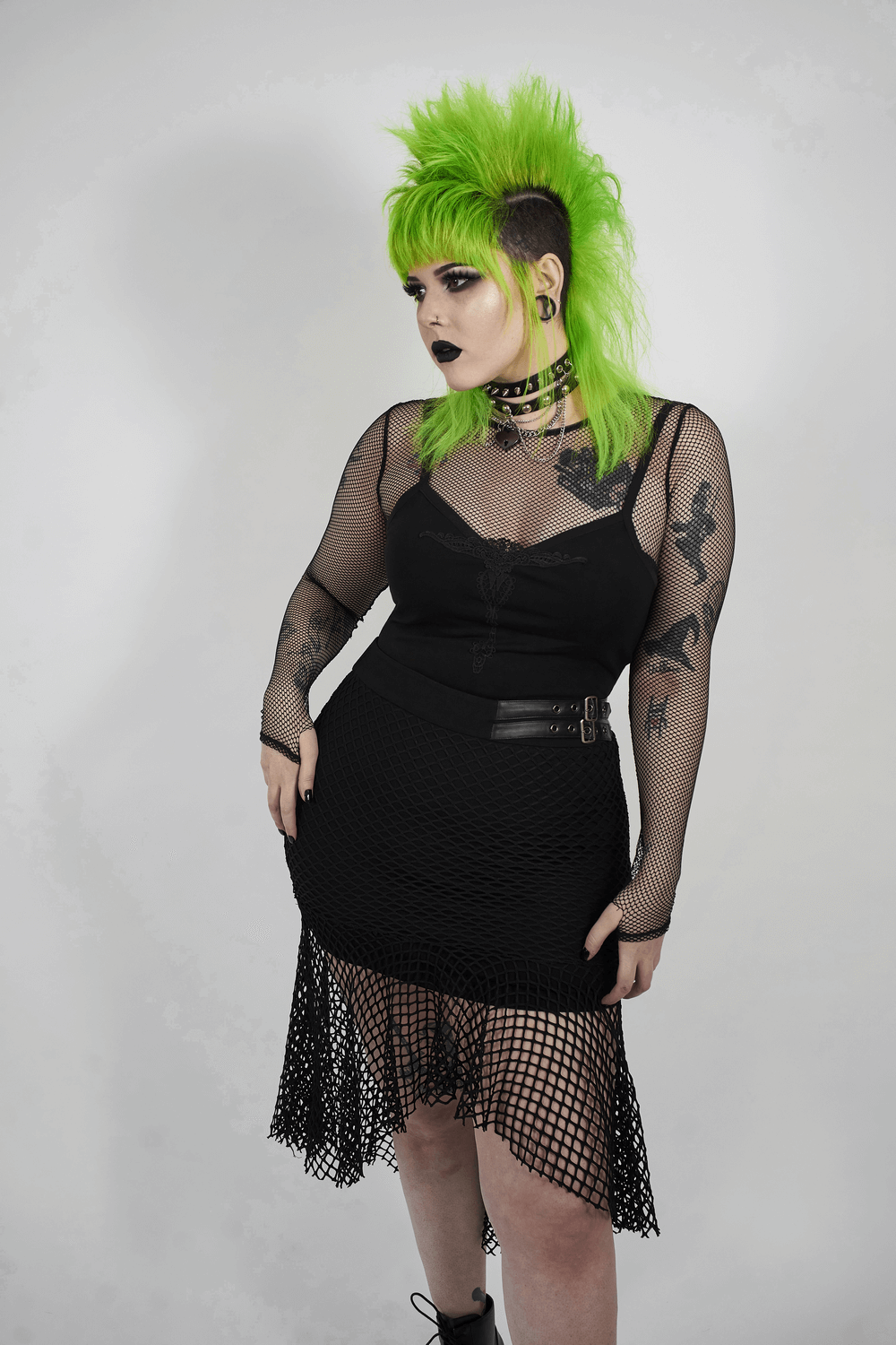 Chic black mesh skirt with buckles and asymmetric hem, stylishly paired with a black mesh top and vibrant green mohawk.