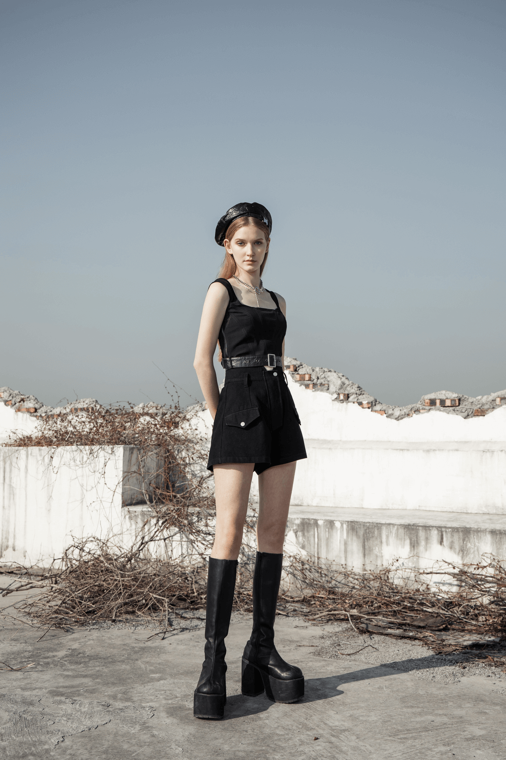 Chic model in a black plaid mesh top with stylish belt and tall black boots, showcasing trendy urban fashion.