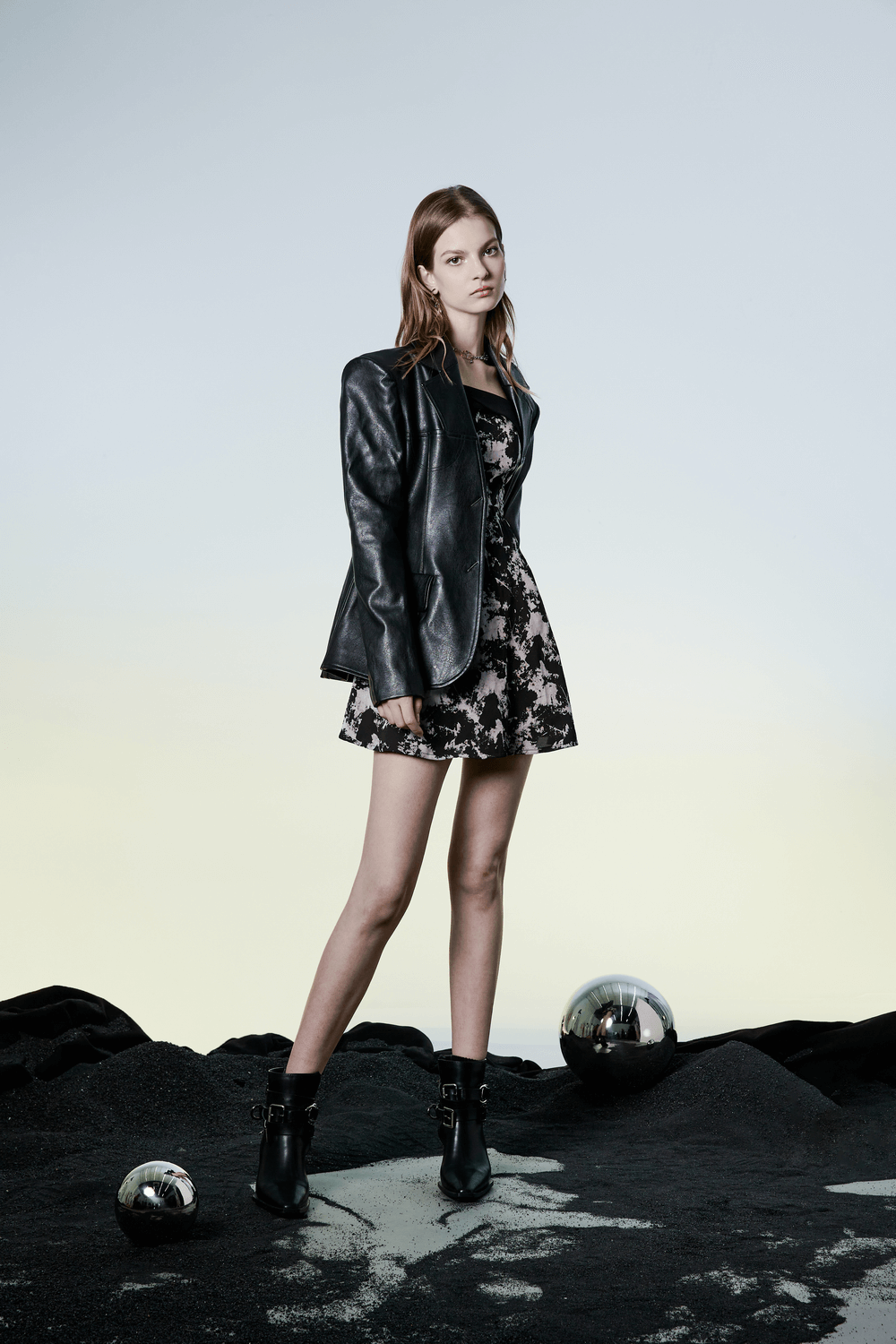 Chic model showcasing a black and white A-line mini dress with abstract design and a stylish leather blazer.