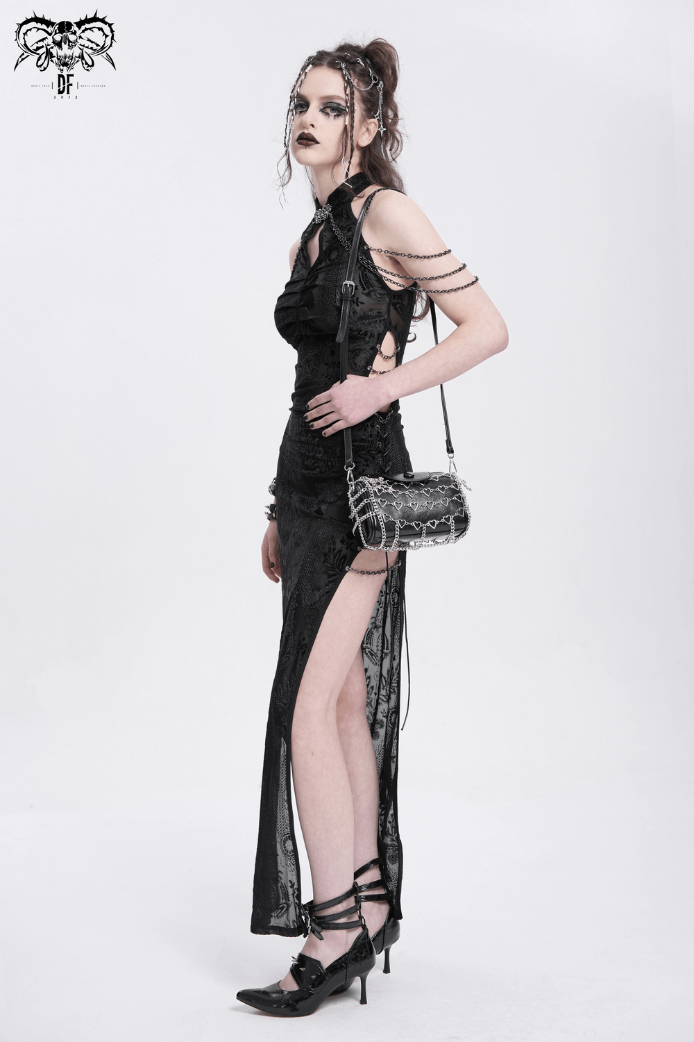 Chic woman in a black dress with a high slit, accessorized with a heart pattern chain crossbody bag.