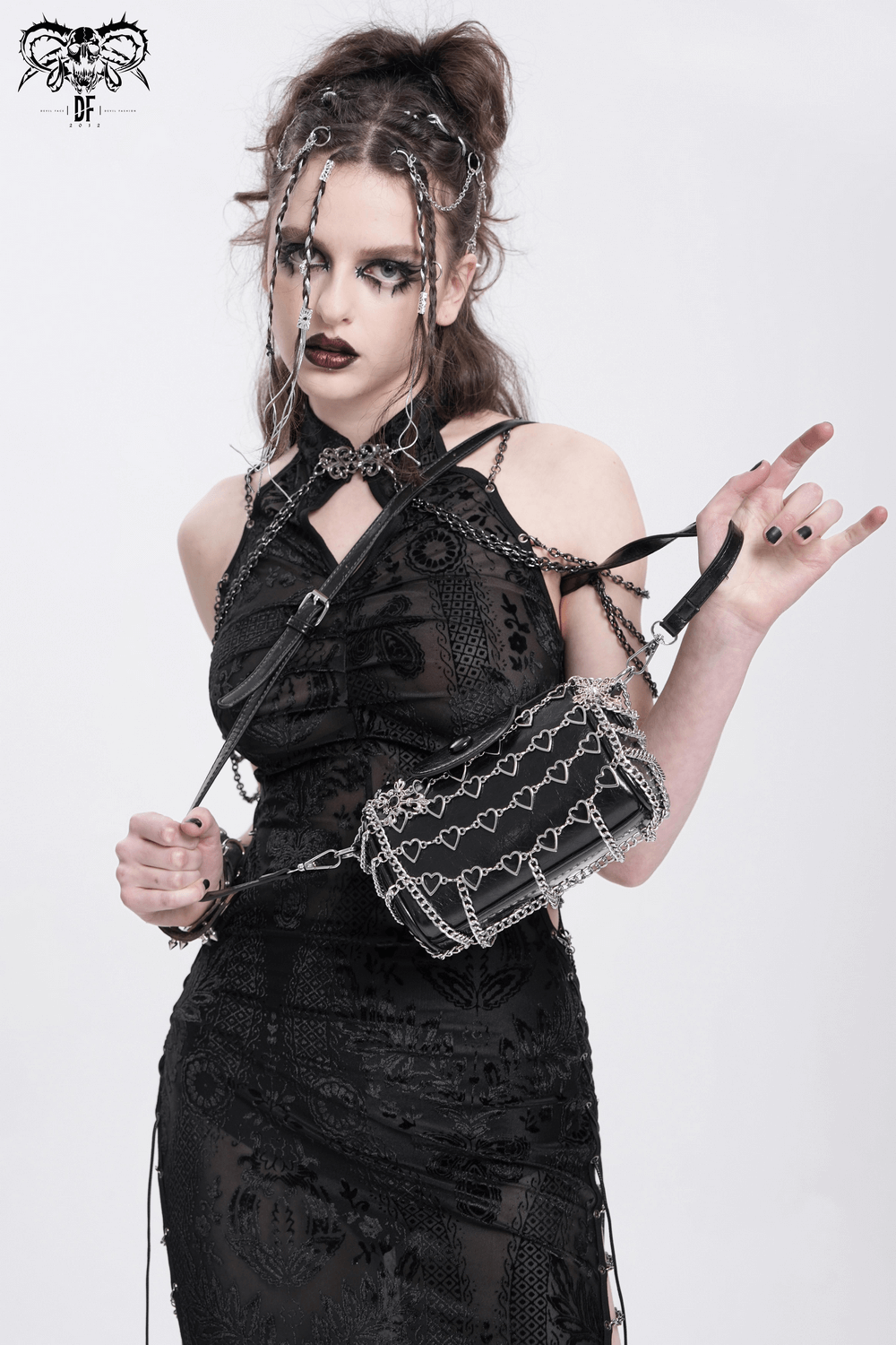 Chic black heart pattern crossbody bag with chains, worn by a stylish woman in a black dress, perfect for edgy fashion.