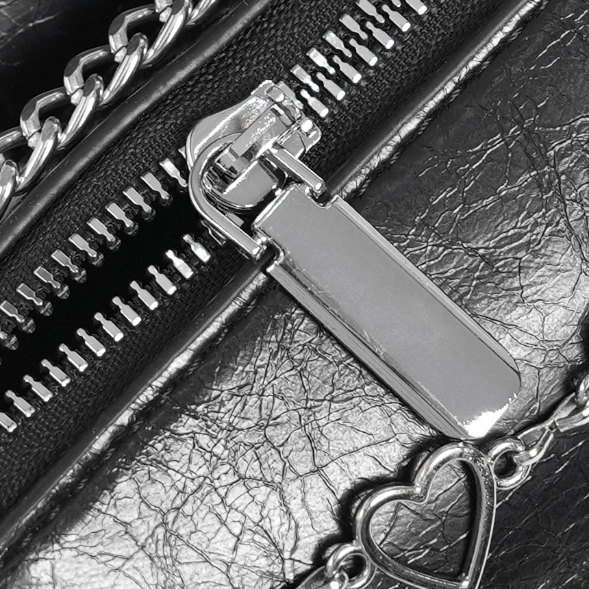 Close-up of the sleek zipper and metallic charm on a chic black heart-pattern crossbody bag for women.