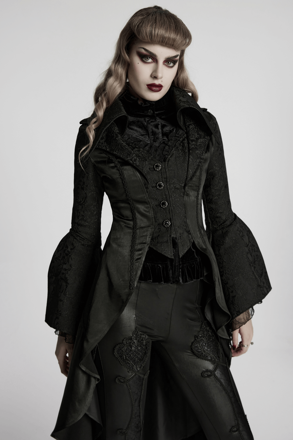 Chic high-low tailcoat in black with jacquard lace and elegant buttons, worn by a model with striking makeup.