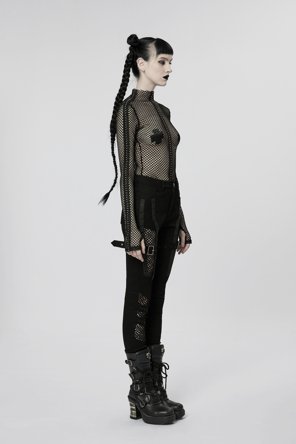 Model in punk mesh and eyelet gothic trousers with edgy black top and chunky boots, showcasing rebellious style.