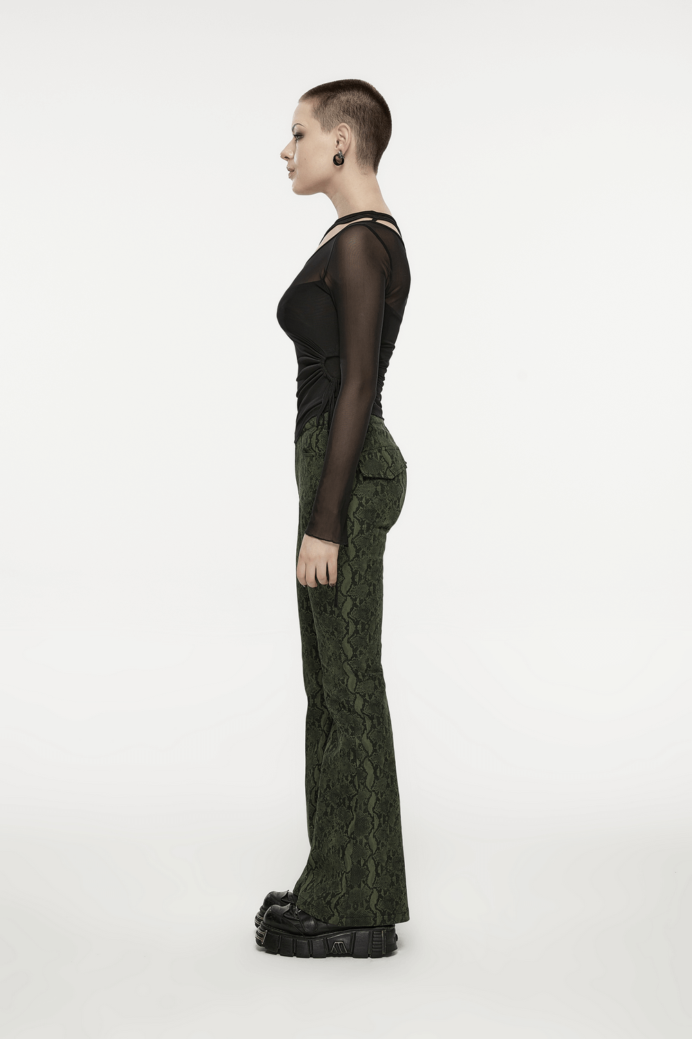 Side view of model in chic black mesh sleeve top with green flared pants, showcasing edgy fashion.