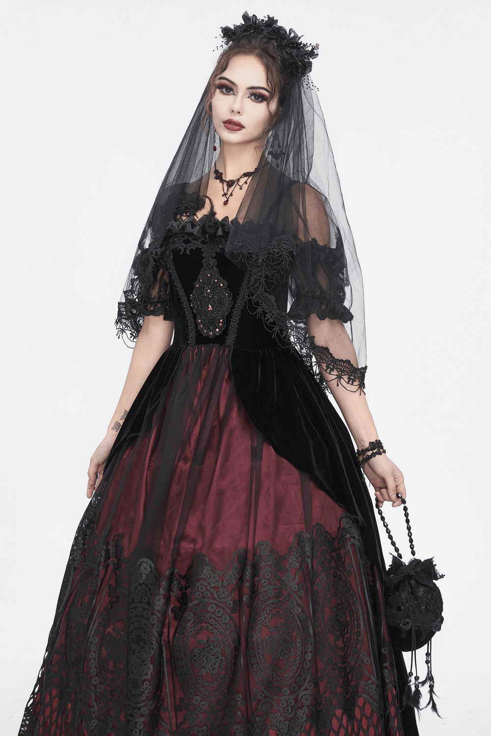 Elegant model in a black and burgundy gown with lace details, wearing a veil and holding a matching handbag.