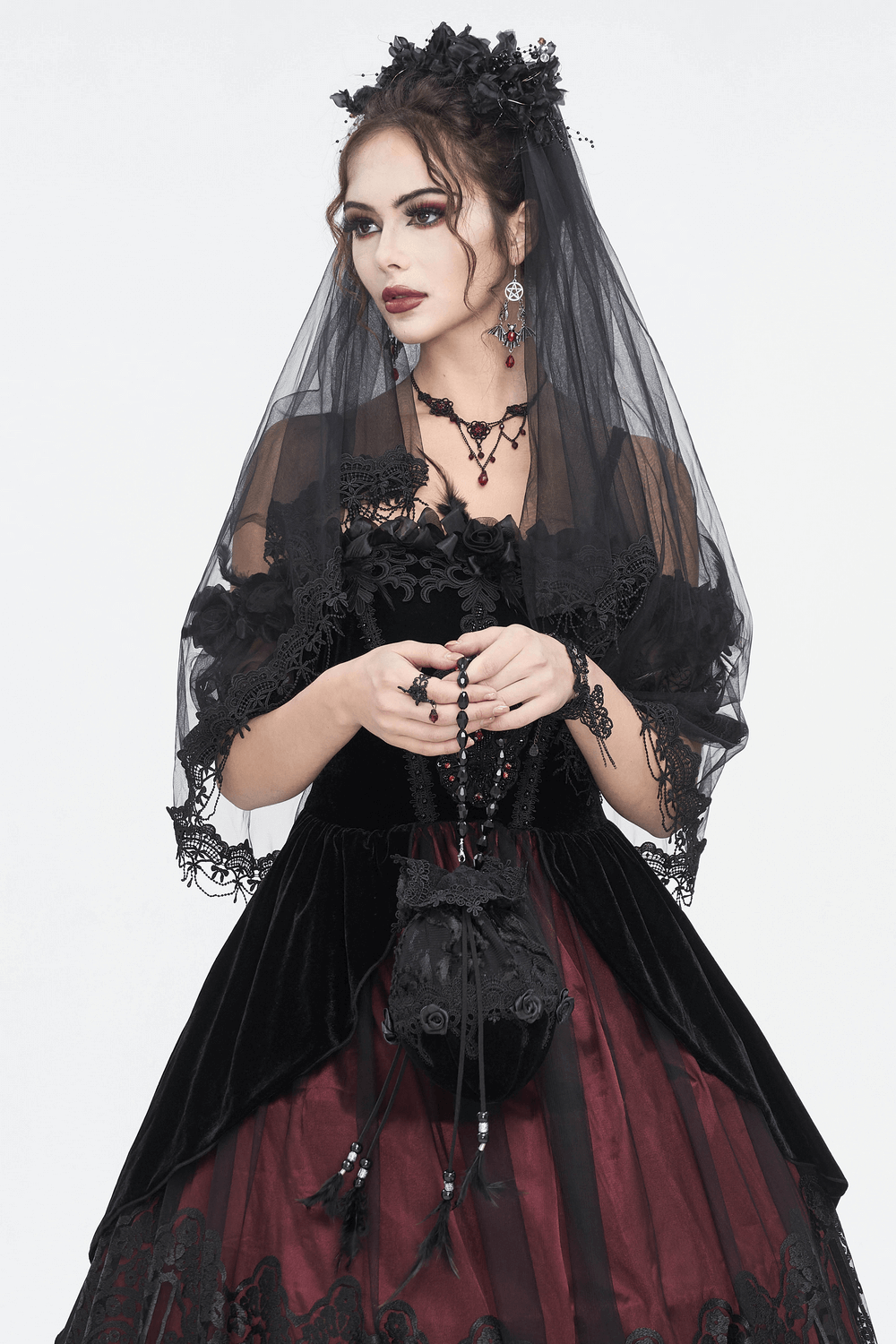 Elegant model in black lace dress with veil holding a black lace evening bag, showcasing gothic style and sophistication.