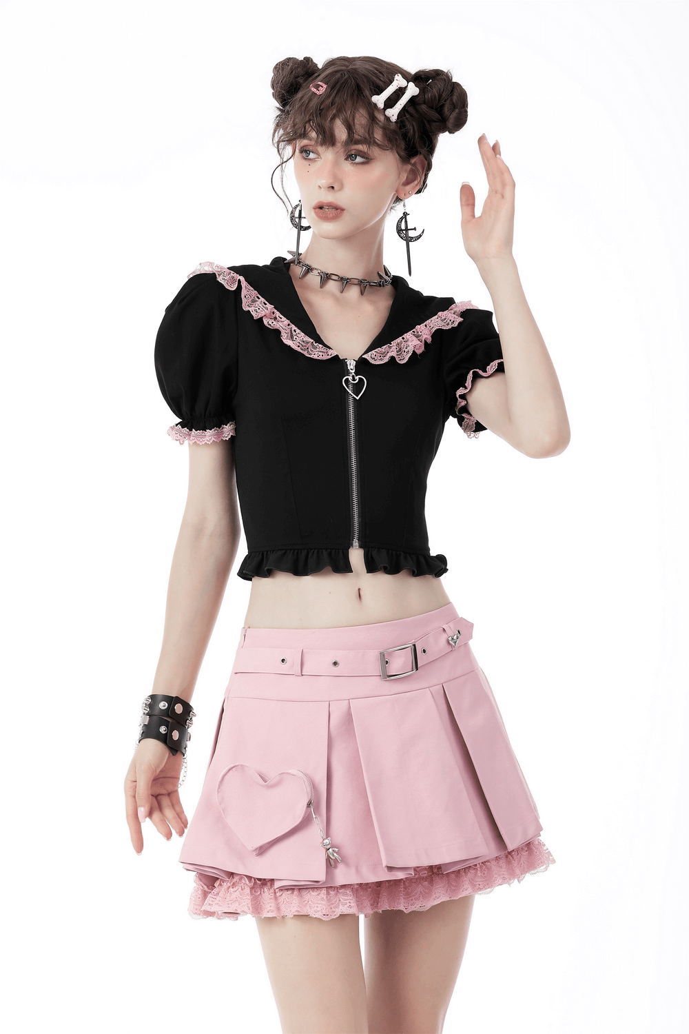 Chic model wearing a black crop top and pastel pink pleated skirt with lace and heart detail, showcasing trendy fashion.