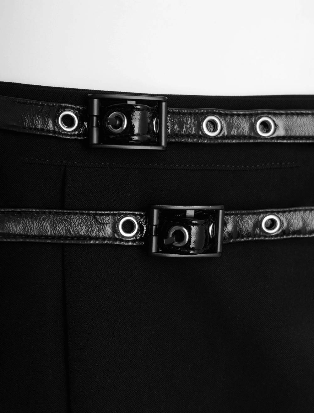Close-up of stylish detachable black waist belts with metal buckle accents for a chic pleated skirt.
