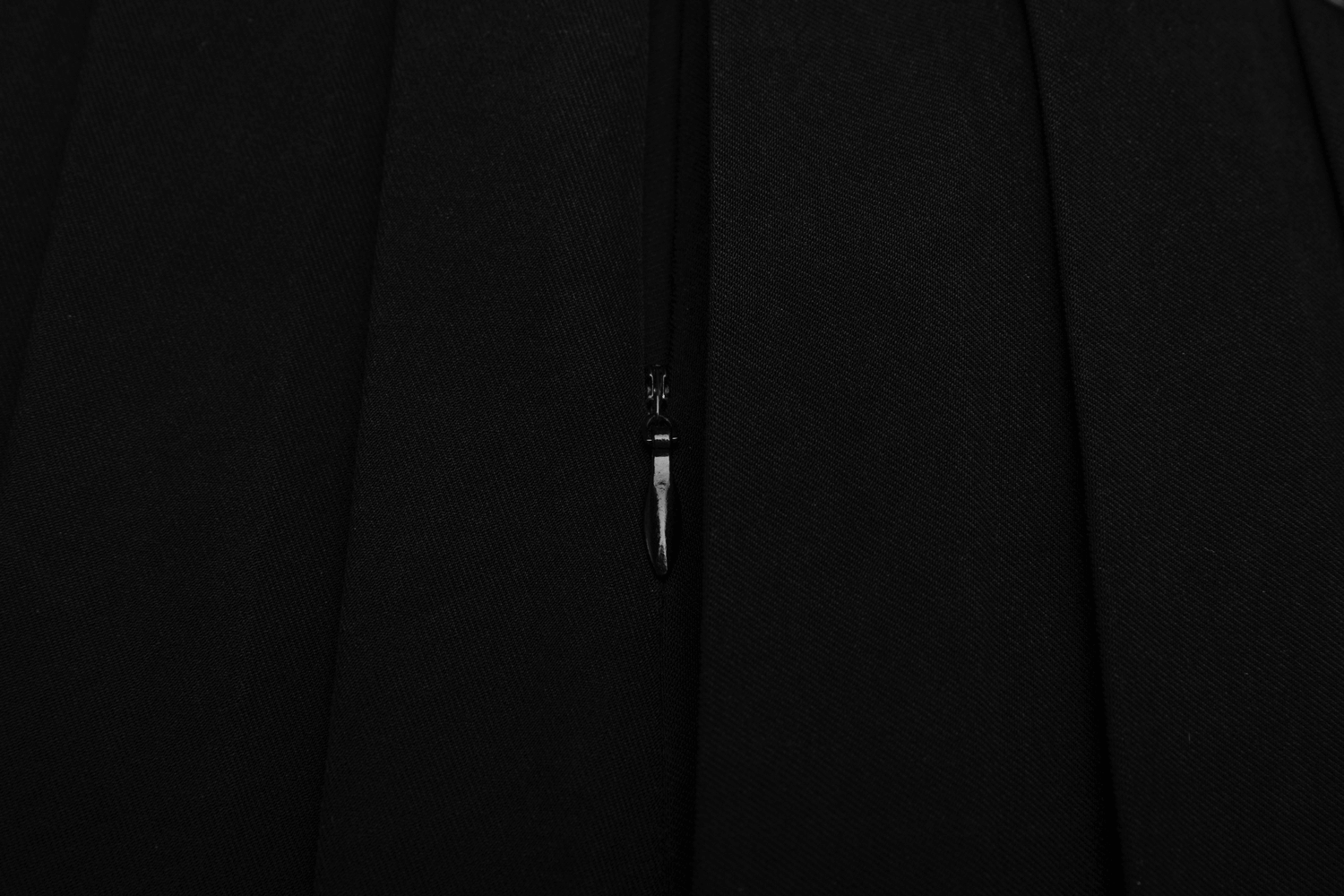 Close-up of the side zipper on a chic pleated skirt, showcasing sleek black fabric and stylish design.