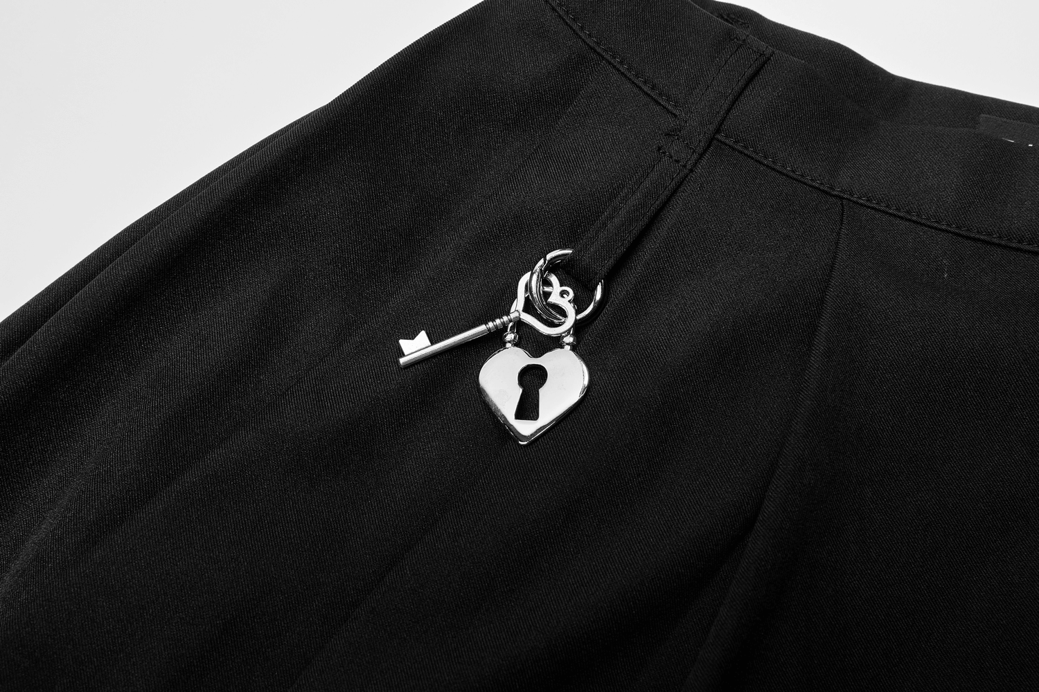 Close-up of a chic pleated skirt featuring a silver heart lock and key pendant for an edgy touch.