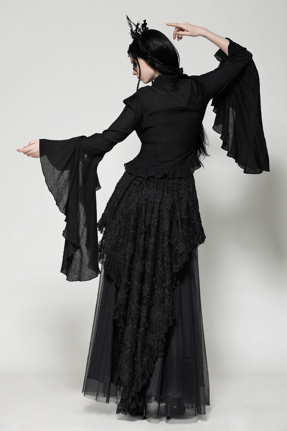 Elegant Gothic black top with dramatic ruffled bell sleeves and lace details, featuring a vintage brooch, worn by model for a back view.