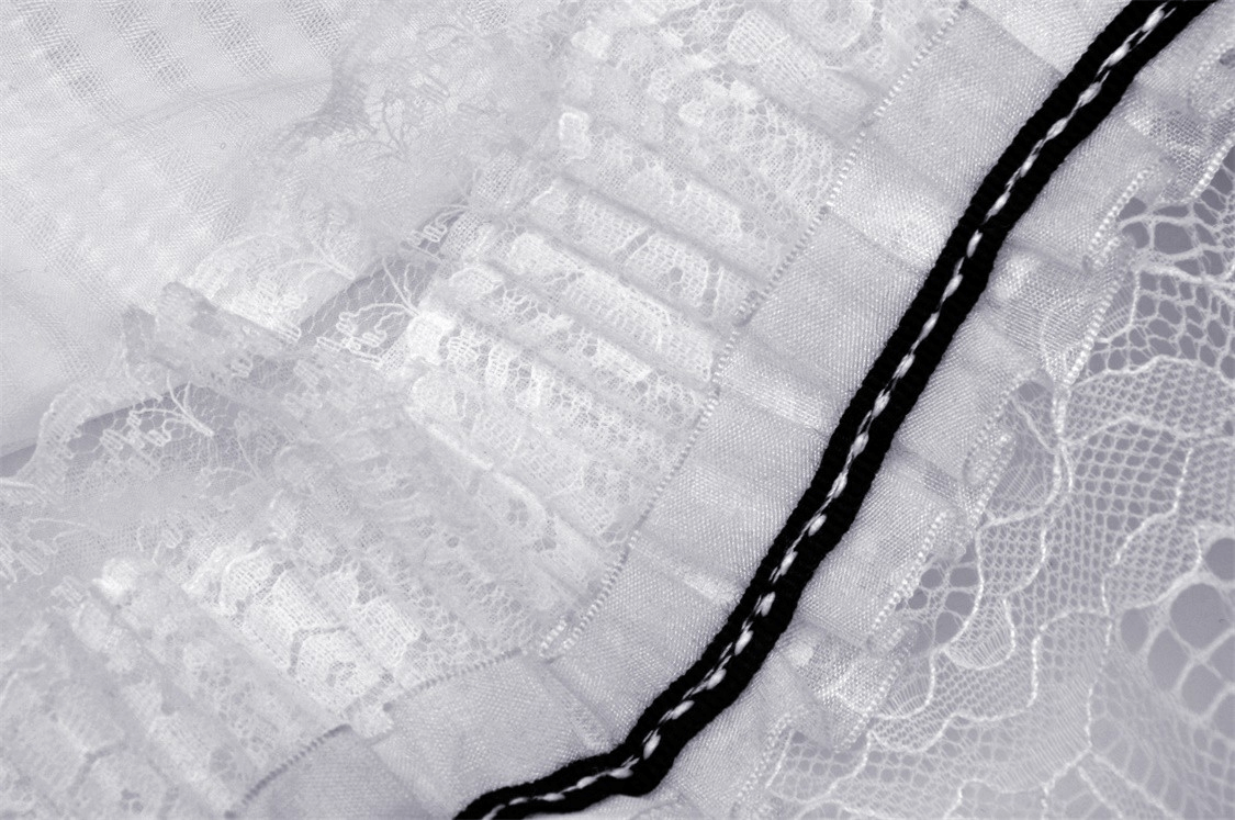 Close-up of white lace trim with delicate ruffles and black ribbon accent, perfect for a chic dress design.