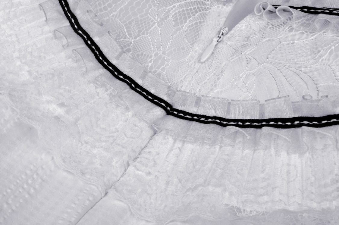 Close-up of lace and ribbon trim on a chic white dress, showcasing elegant details and refined craftsmanship.
