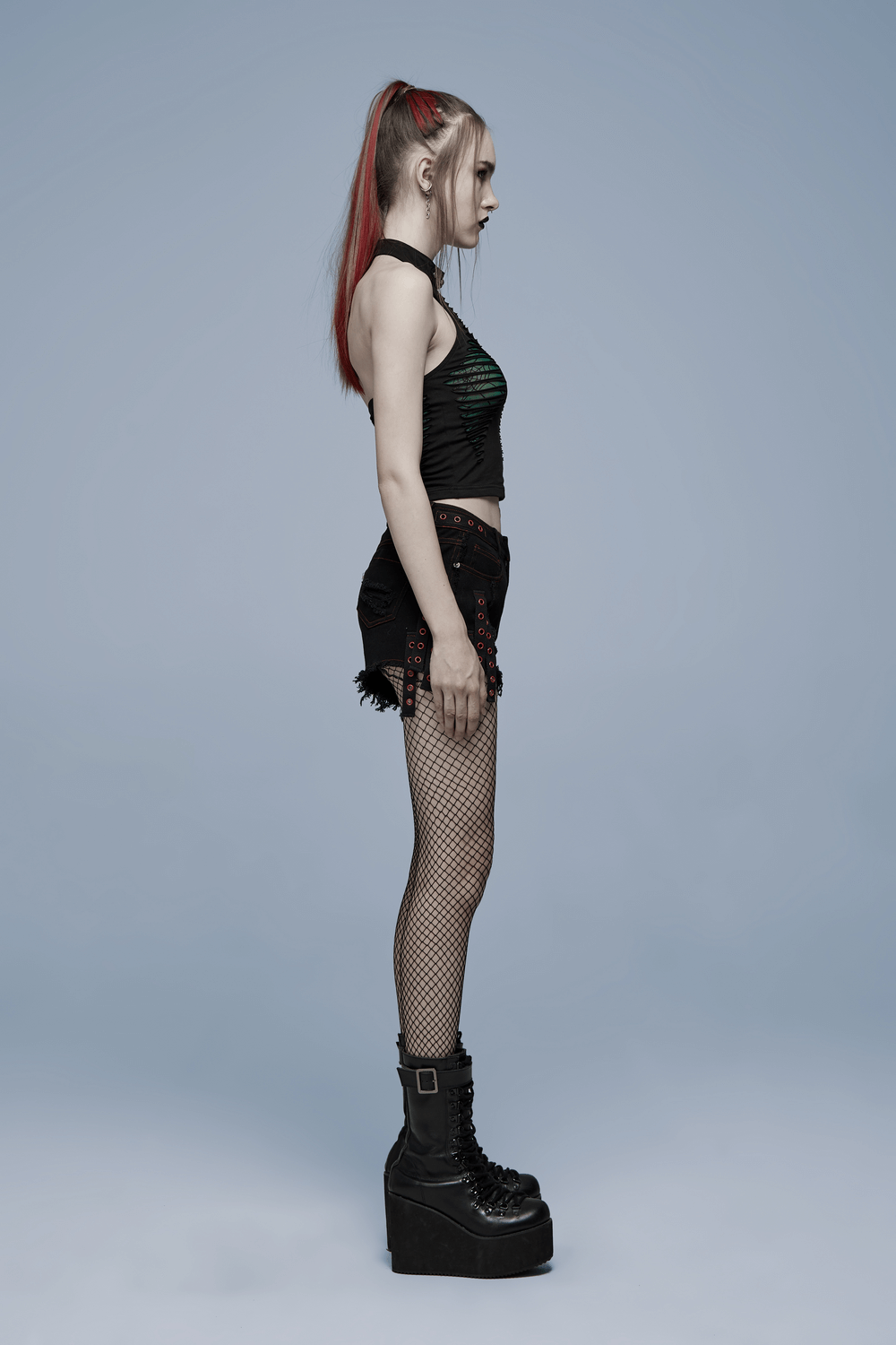 Model in edgy spider mesh cut-out halter top, showing side profile with platform boots and fishnet shorts.