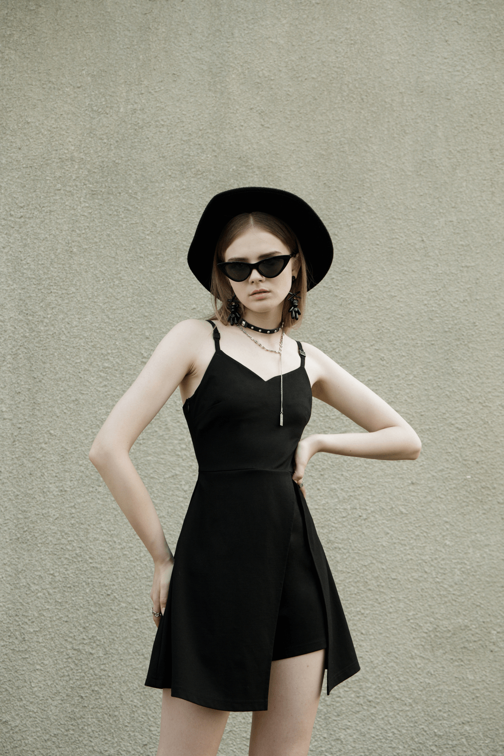 Chic black V-neck dress with high slit and detachable shorts, styled with sunglasses and a hat.