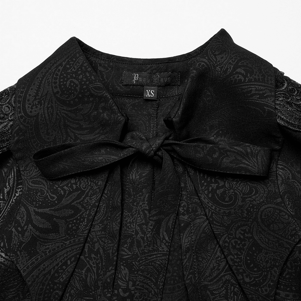 Close-up of black chiffon lapel cloak with ornate paisley print and bow tie detail, showcasing goth fashion style.