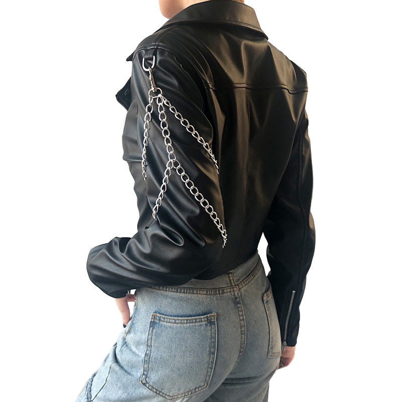 Back view of a women's black faux leather motorcycle jacket with chains, styled with denim jeans.