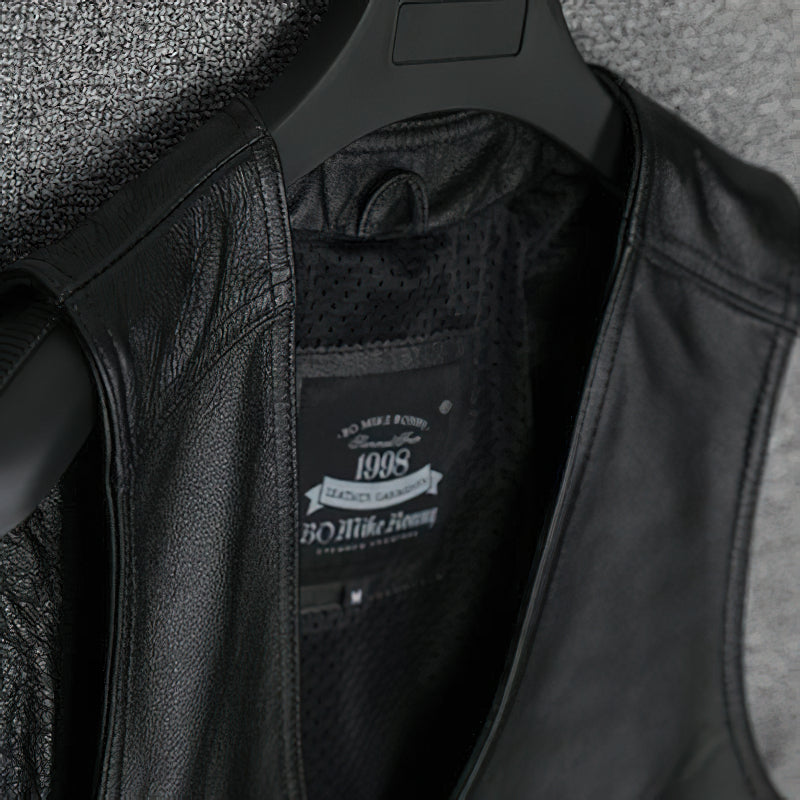 Close-up of collarless black leather vest interior, featuring tag and breathable lining for biker style.