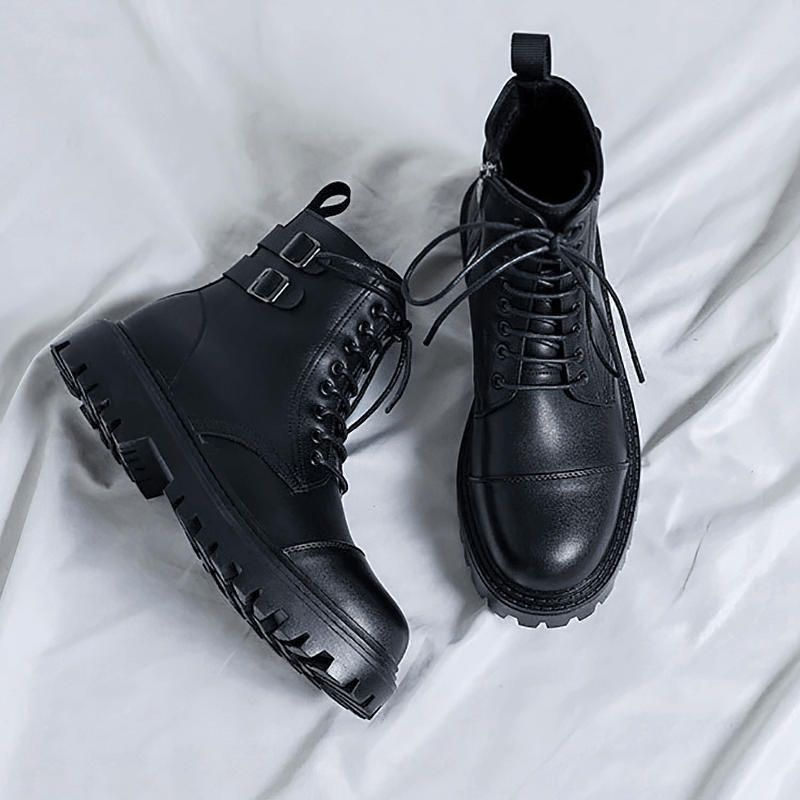Men's black lace-up ankle boots with stylish buckles and a comfortable rubber sole on a soft backdrop.