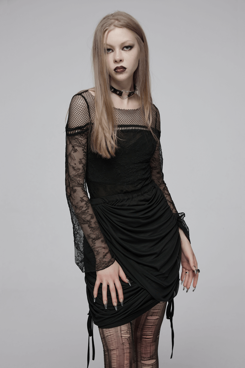 Model in a black lace and mesh dress with asymmetrical draping, showcasing a gothic fashion statement.