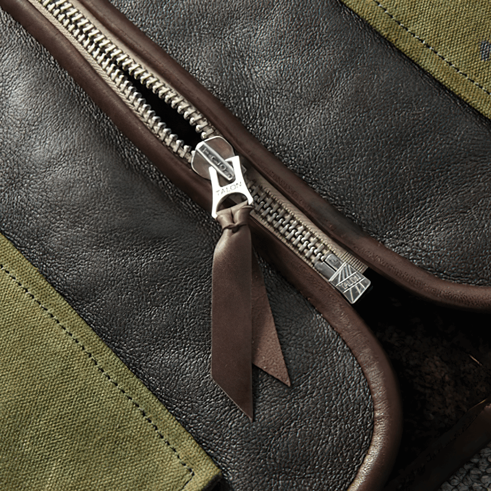 Close-up of zipper on black leather biker vest with green pockets, showcasing quality craftsmanship and design.