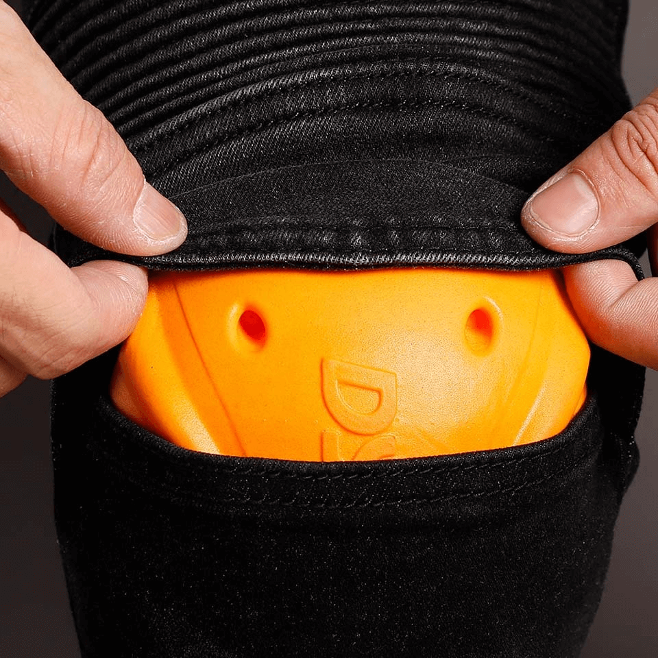 Close-up of hands revealing protective orange insert in black motorcycle pants for added safety.