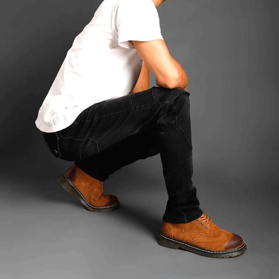 Man in protective biker jeans squatting, showcasing stylish brown boots and a casual white t-shirt.