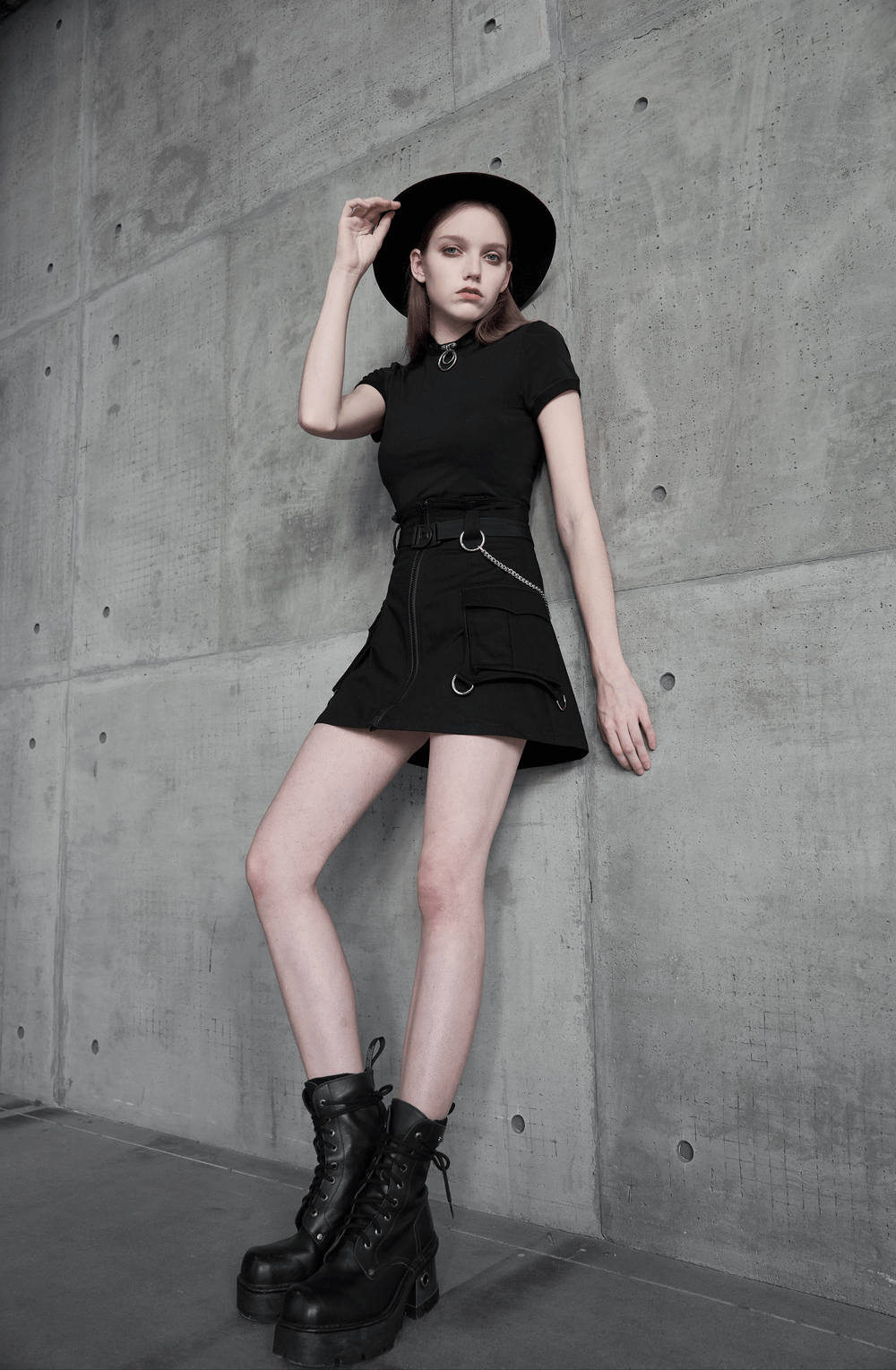 Model showcasing a black A-line denim skirt with chains, styled with a hat and combat boots in an urban setting.