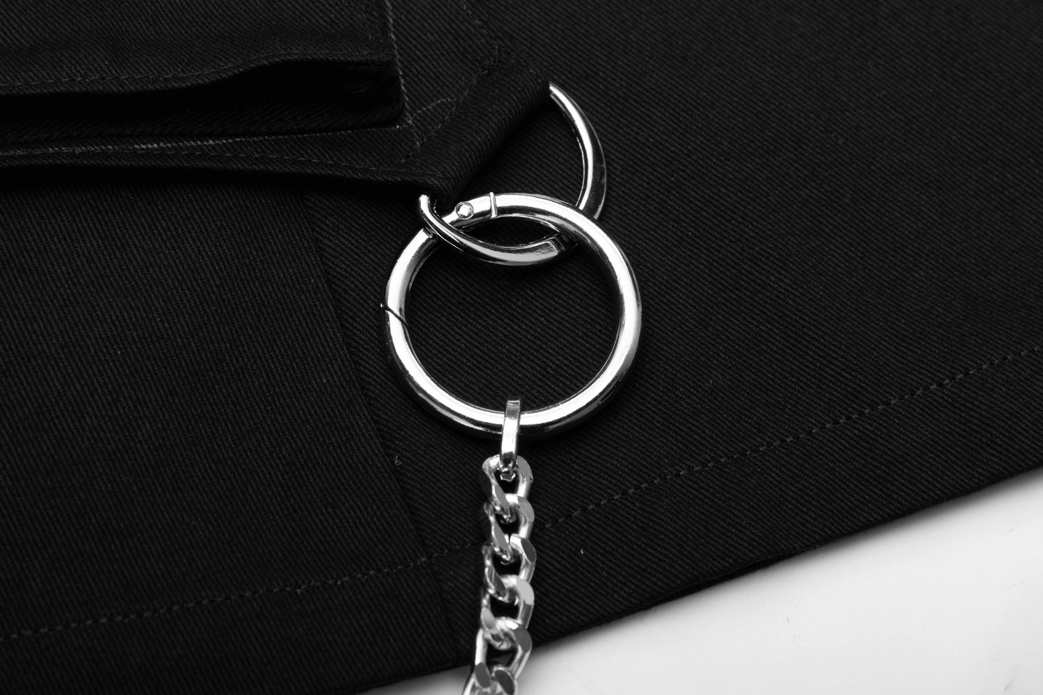 Close-up of a silver chain and ring detail on a black denim skirt, perfect for a cyberpunk look.