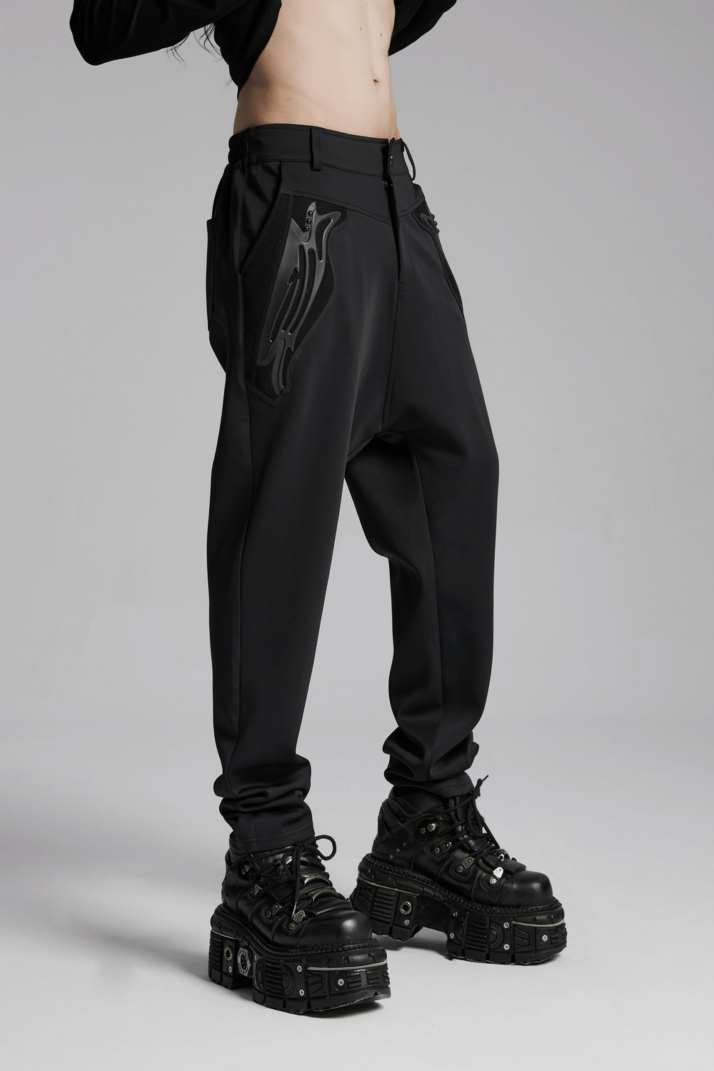 Cyberpunk knitted pants with rivets, 3D pocket details, and edgy draped fit, styled with chunky black platform boots.