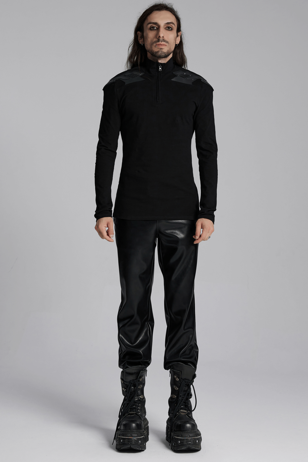 Cyberpunk male model wearing a black tactical top with shoulder patches and a zipper, paired with sleek black pants.