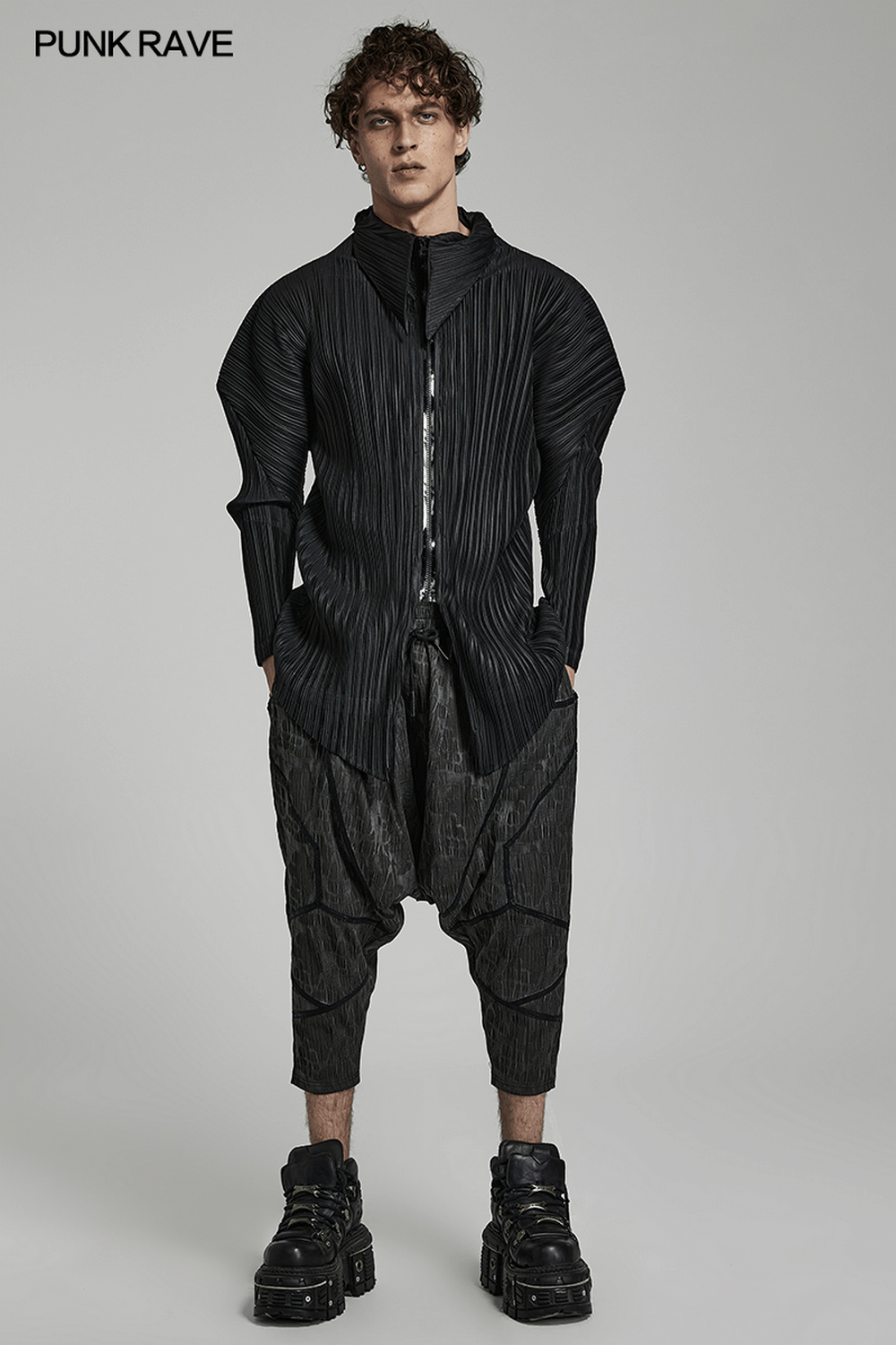 Stylish man in black layered drop-crotch pants and textured jacket, showcasing cyberpunk fashion.