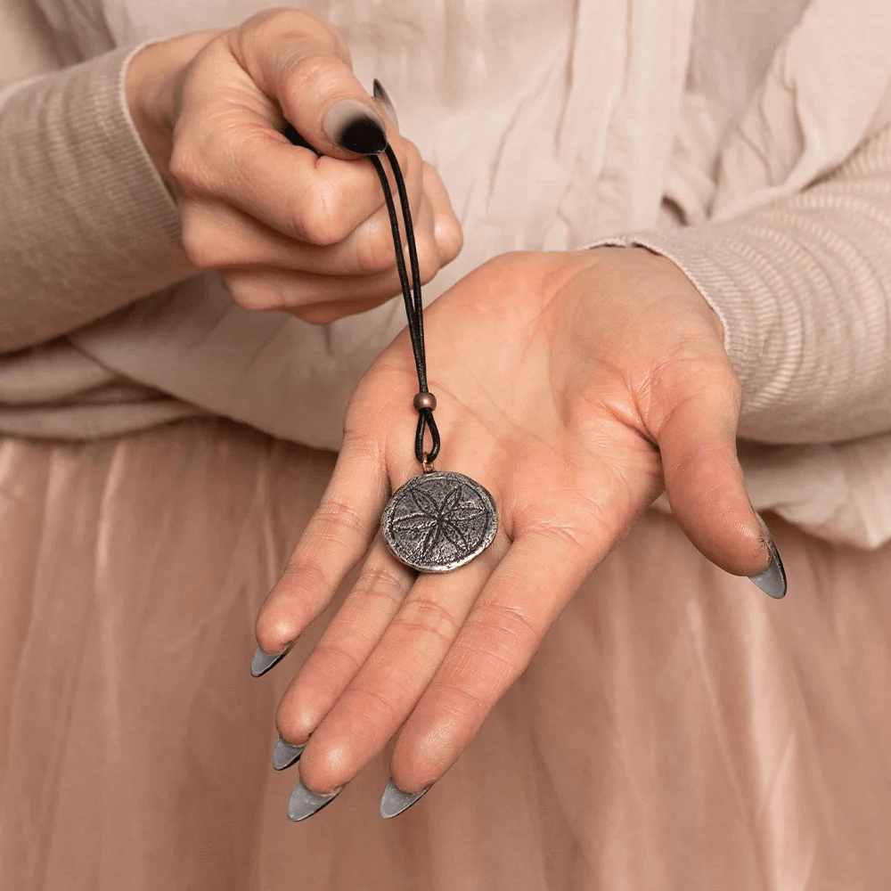 Daisy Wheel Pewter Amulet Gothic Protection Necklace held in a hand with a black cord, showcasing its intricate design.