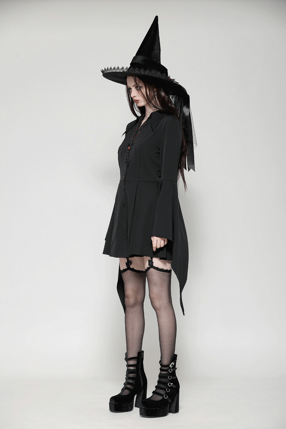 Woman in a dark goth dress with corset back and witch hat, showcasing a gothic and alternative fashion style.