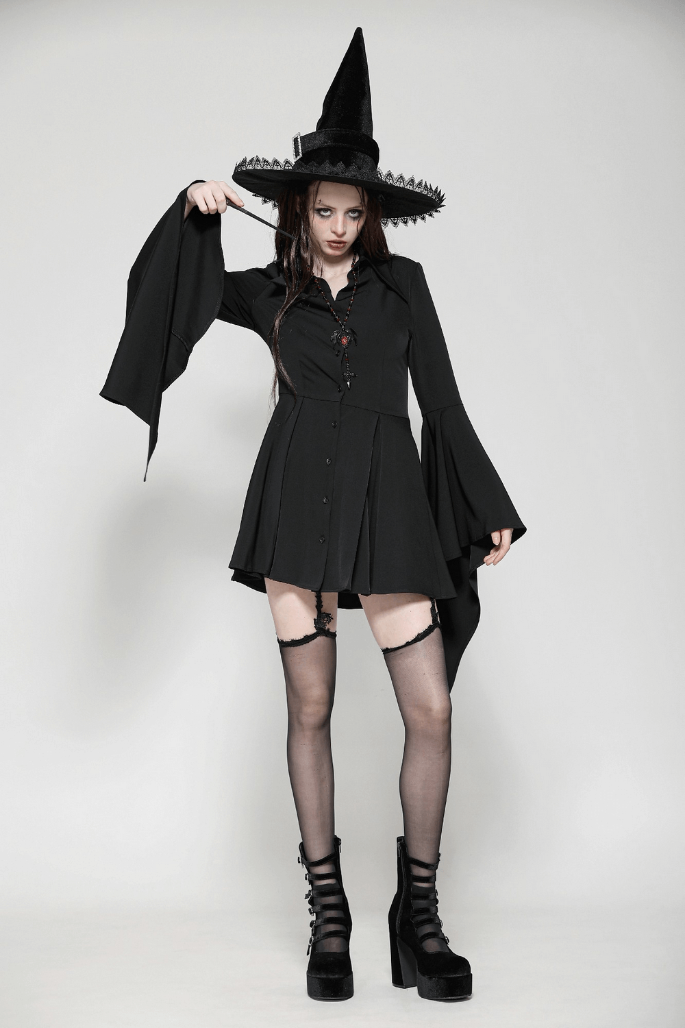 Gothic black dress with flared sleeves, lace-up back, and pointed collar, paired with a witch hat and platform shoes.