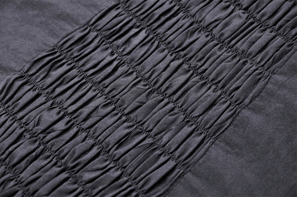 Close-up of dark fabric with smocked detailing, showcasing textured black material for fashion design.